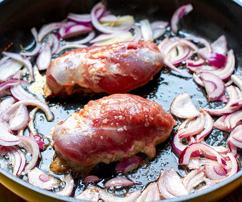 pan frying duck breast in a pan with onions