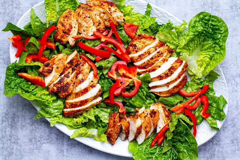 Arranging a Cobb salad on a plate with lettuce, chicken and peppers