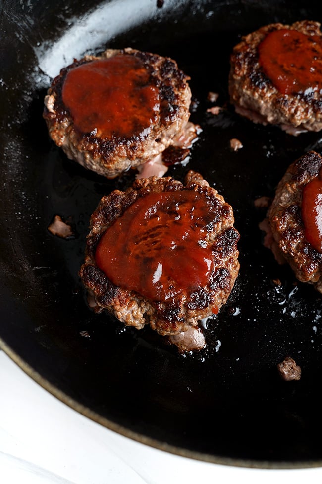 Ketchup spread over beef patties in a frying pan