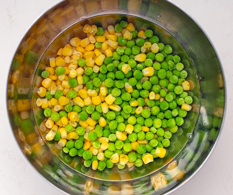 Frozen peas and corn in a bowl with boiling water