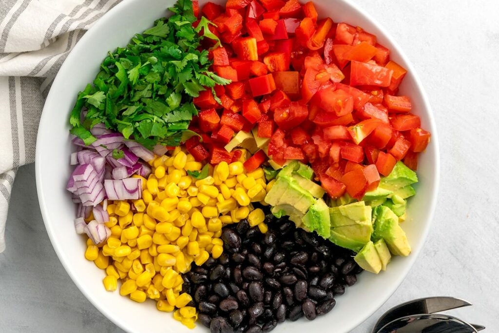 Black beans, corn, avocado, red onion, cilantro, red peppers and tomatoes in a bowl