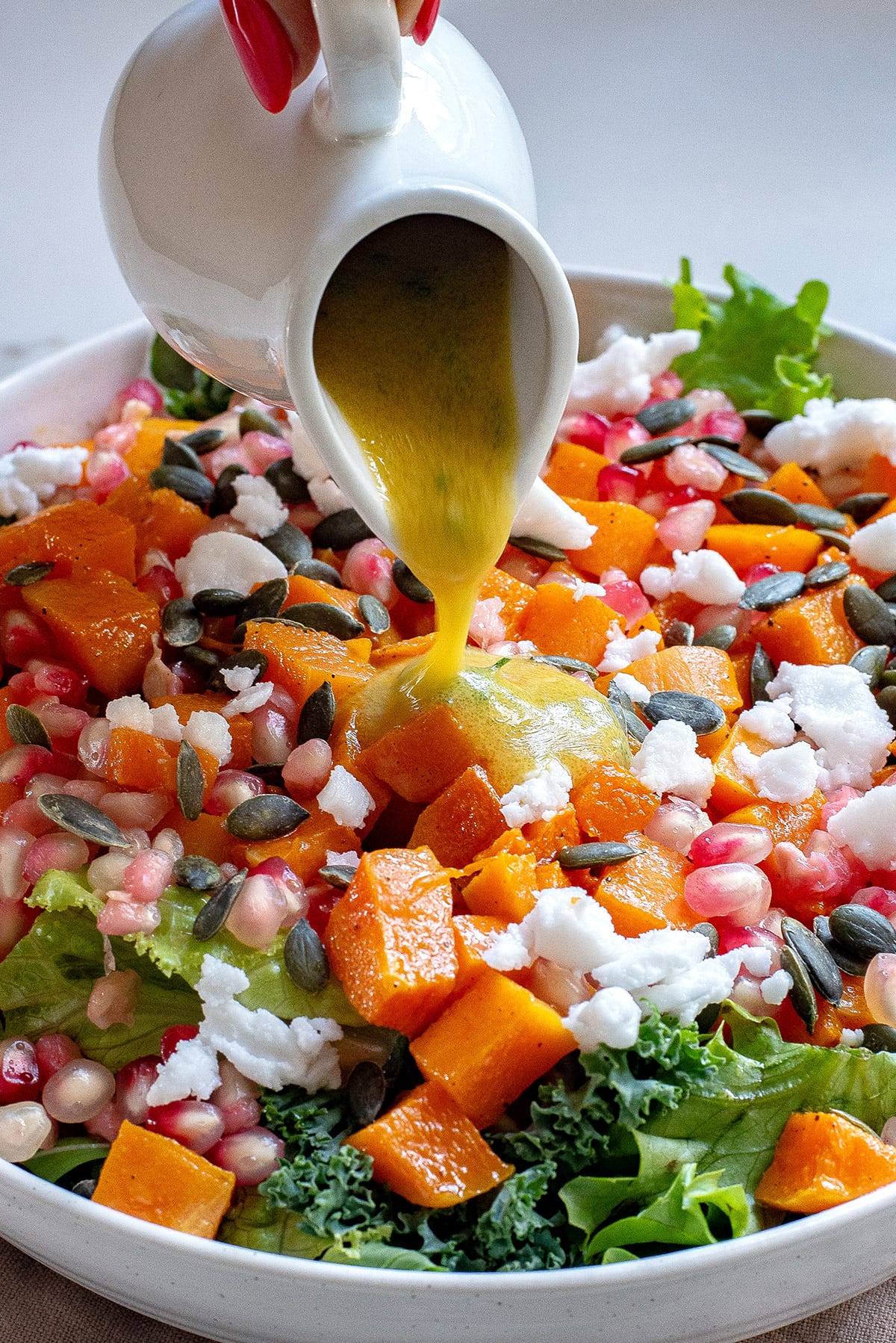 Pomegranate salad with butternut squash with the dressing being poured over the top.