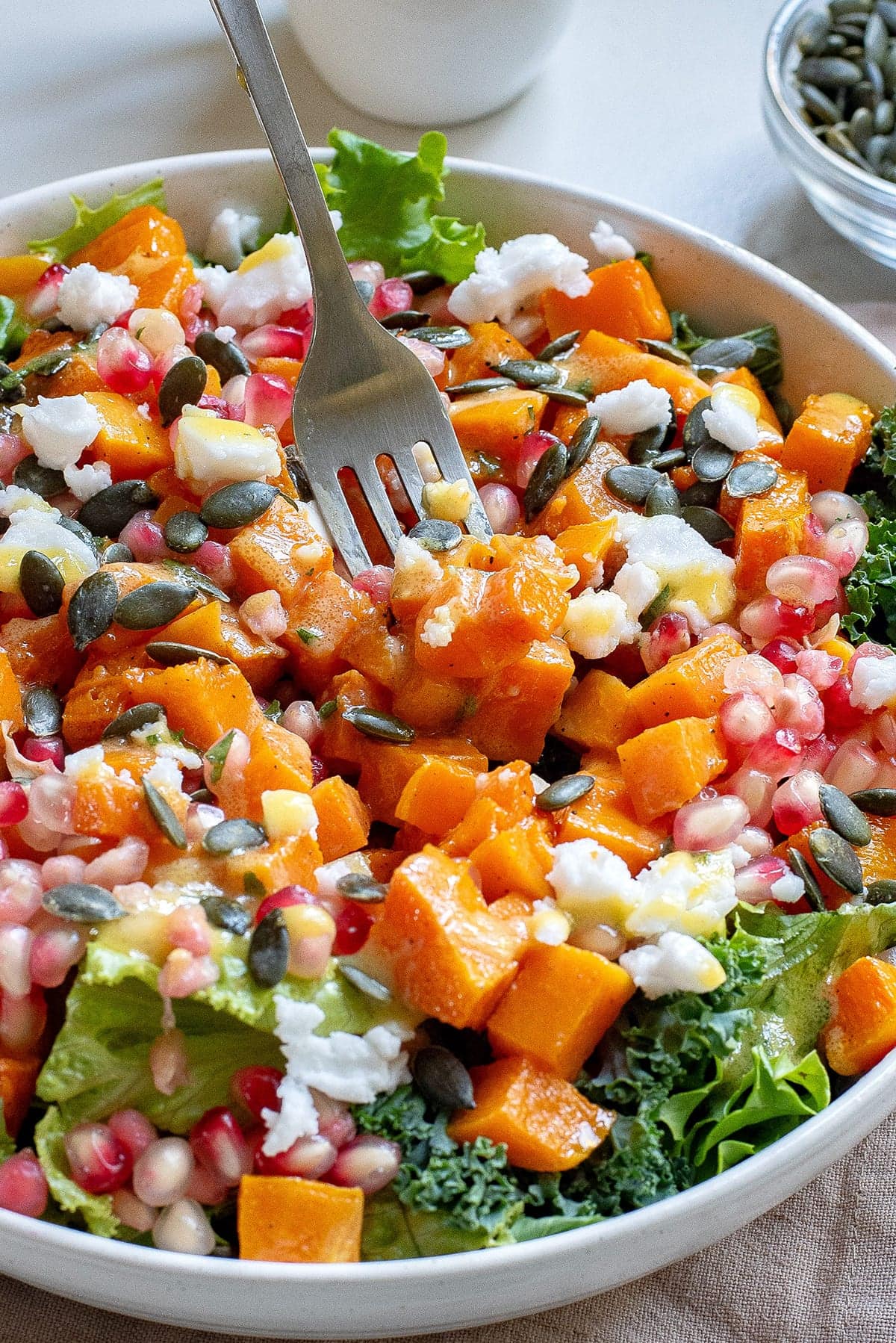 A fork picking up butternut squash cubes out of the winter fall salad.