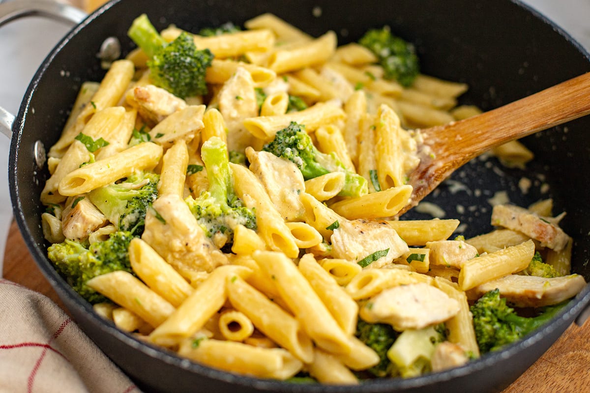 Chicken Broccoli Alfredo pasta stirred with a spatula in a skillet.