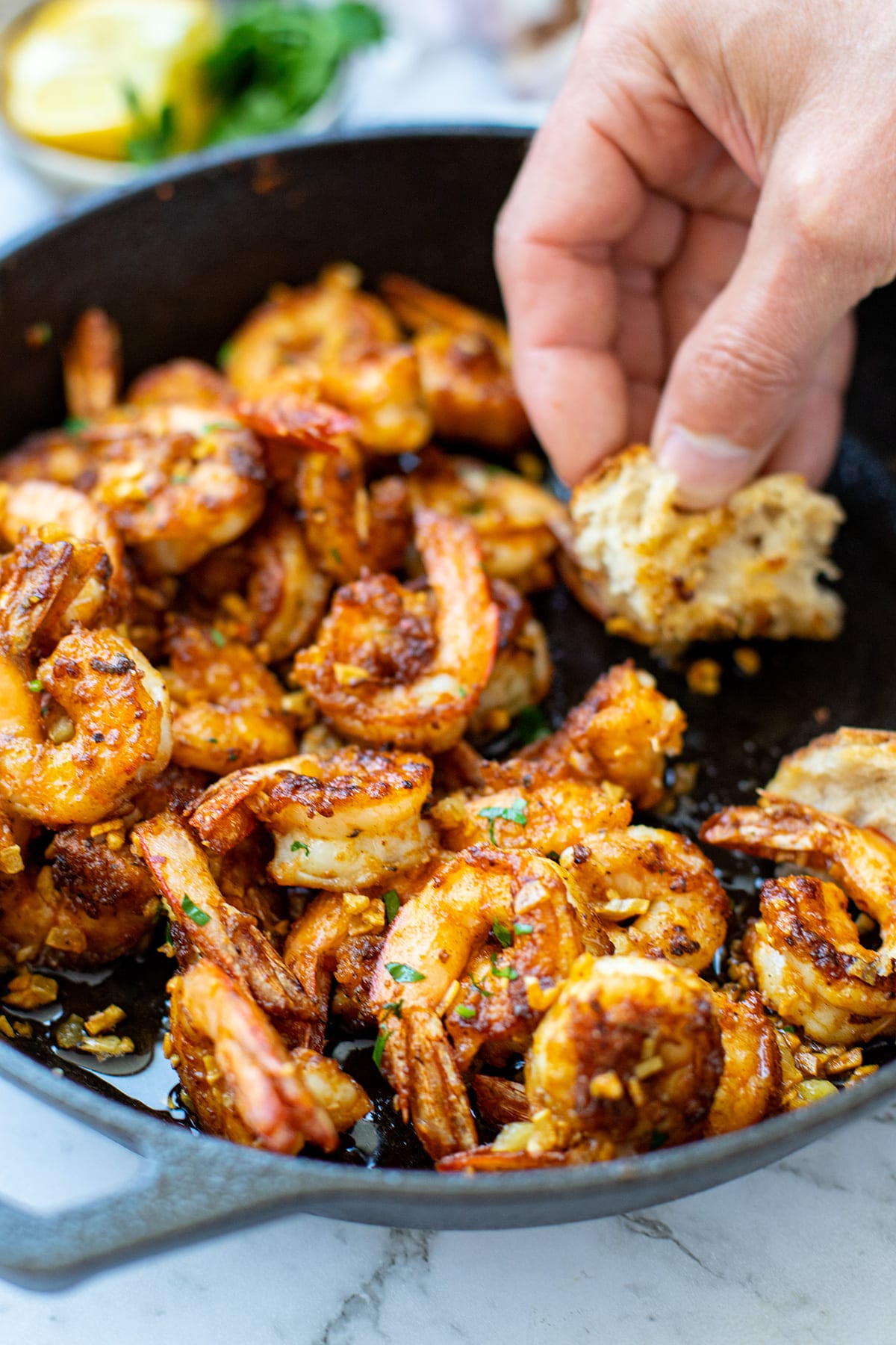 Crispy garlic prawns in a skillet with bread mopping up the sauce.