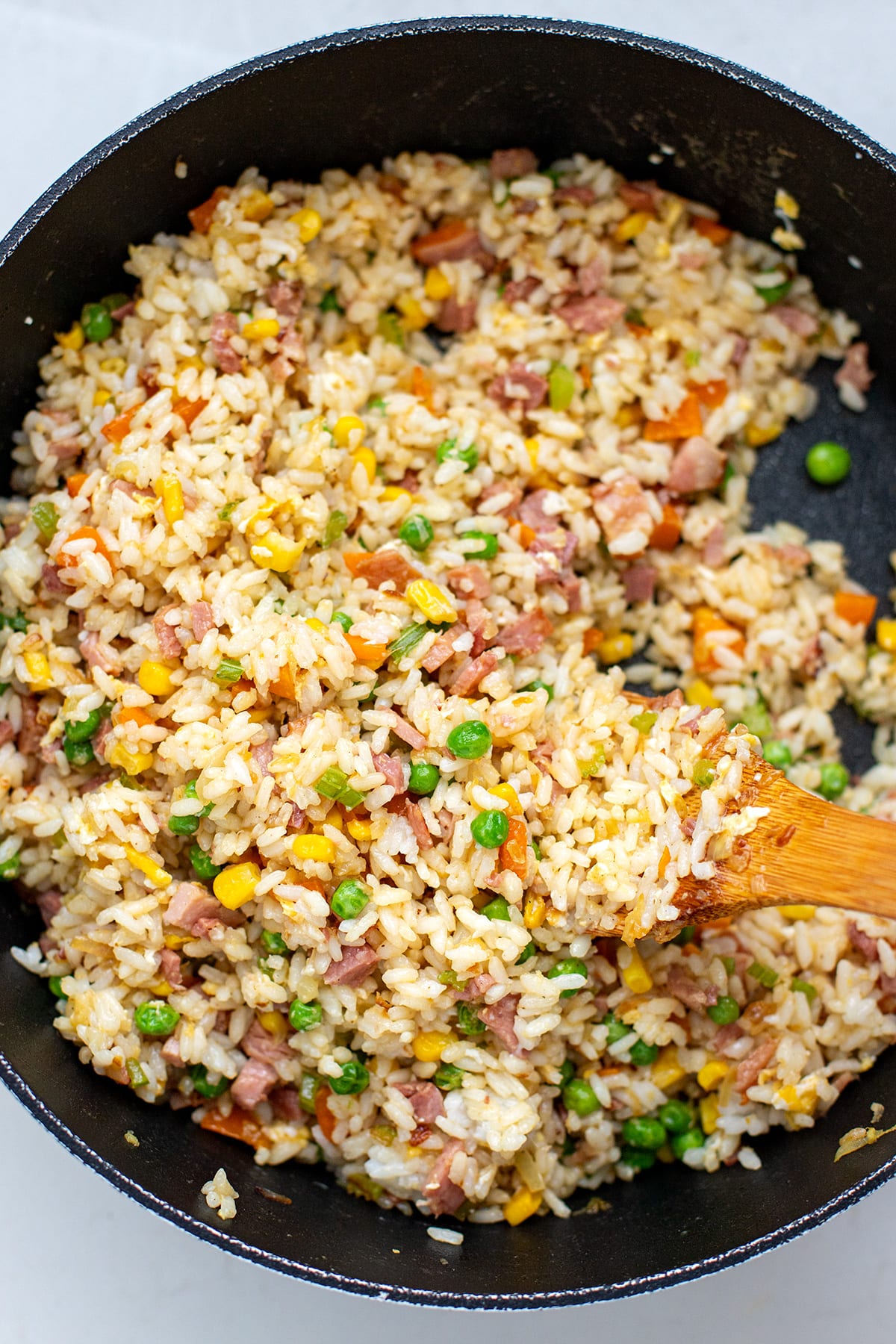 ham fried rice in a skillet with a wooden spatula.