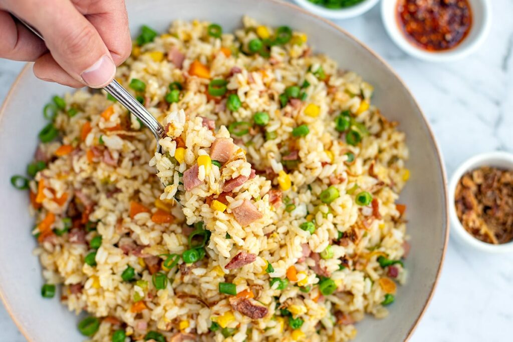 A fork filled with fried rice with ham and vegetables