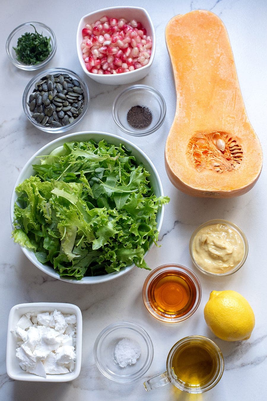 ingredients for fall and winter salad with butternut squash, pomegranate, pumpkin seeds, leafy greens, feta, honey mustard dressing.