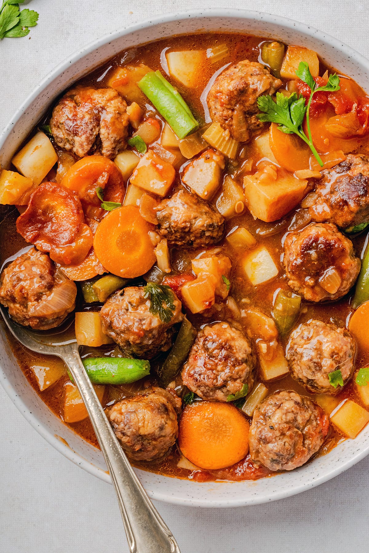 Meatball Stew recipe with potatoes and vegetables in a serving bowl with a spoon