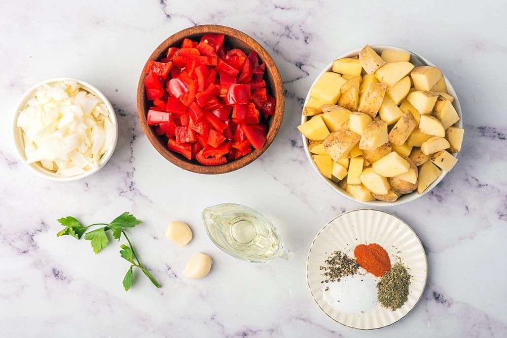 ingredients to make country potatoes: onion, red peppers, potatoes, garlic, olive oil, salt, pepper, thyme, paprika, parsley