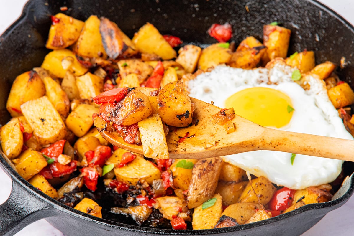 country fried potatoes in a skillet with fried egg and a spatula