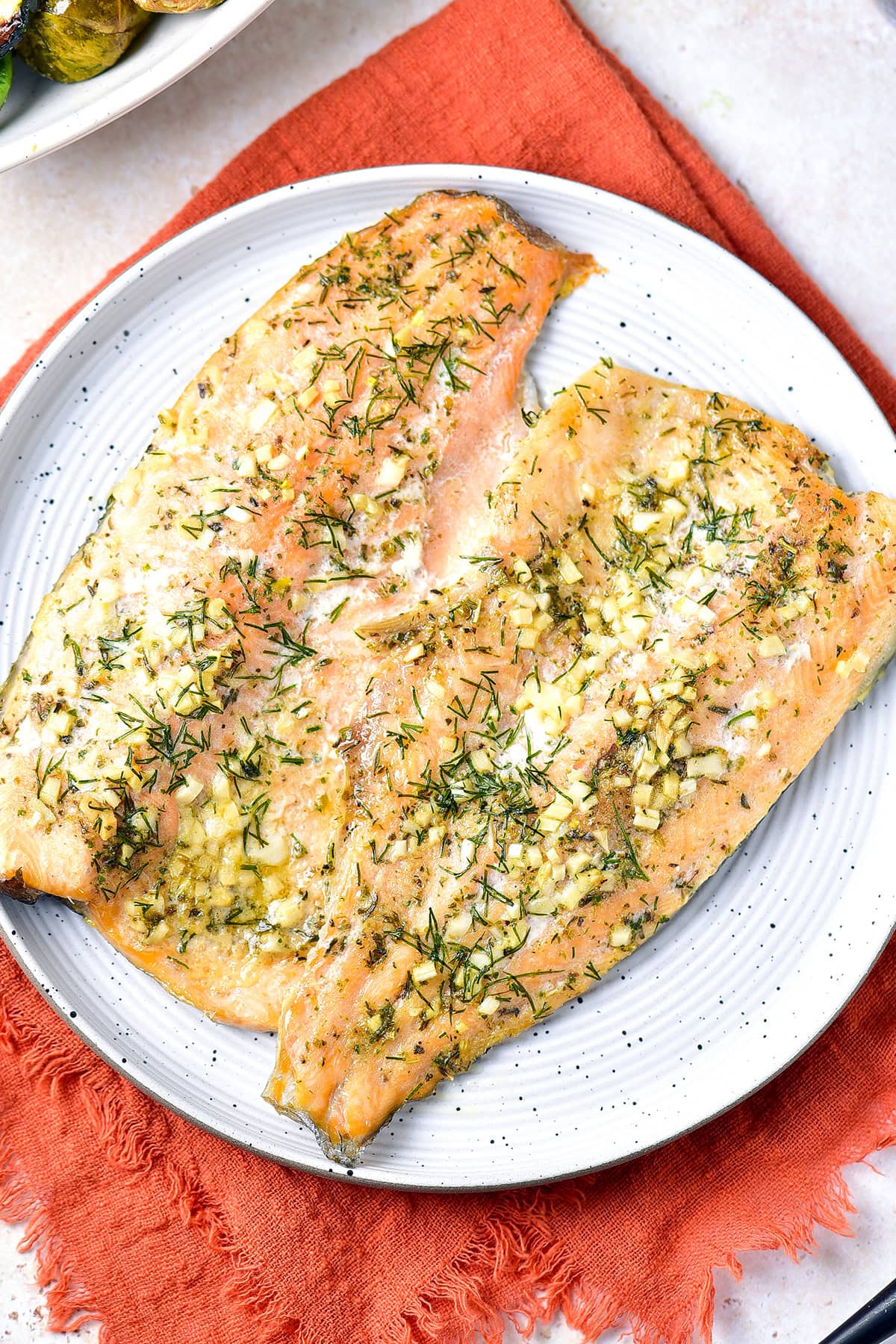 Baked rainbow trout with garlic butter and herbs on a plate vertical image