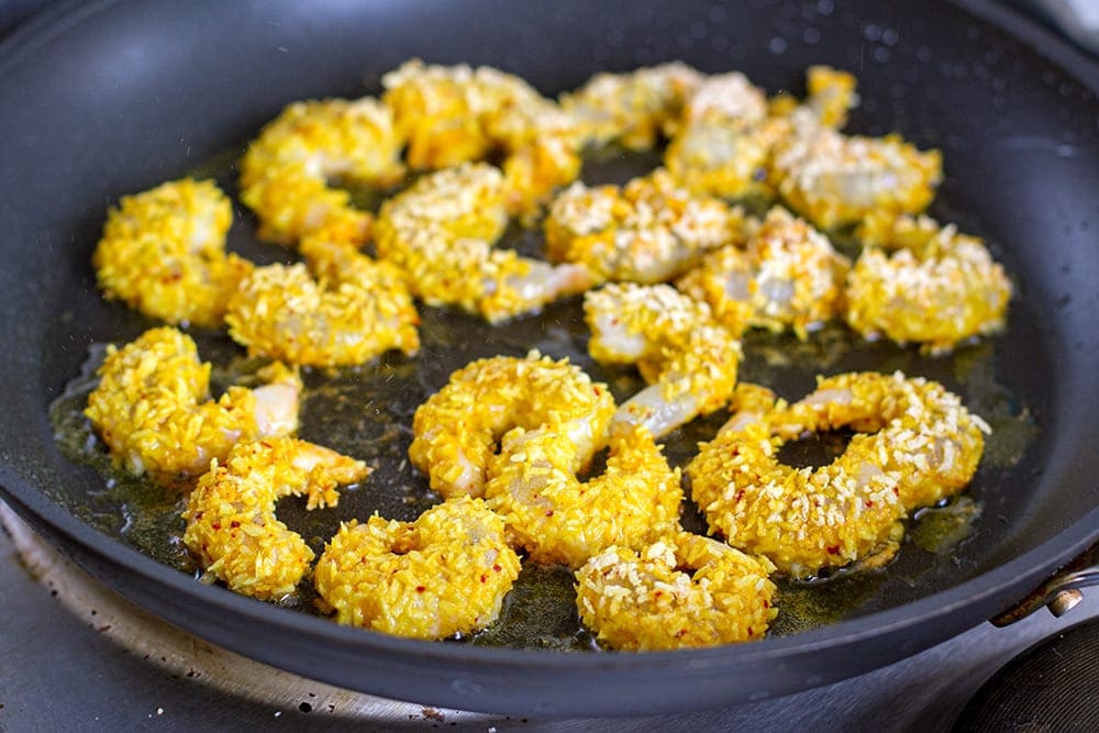 pan frying coconut shrimp in a skillet