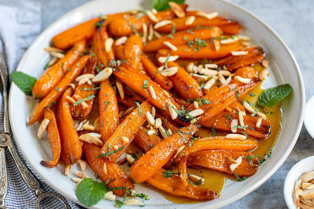 Roasted maple carrots topped with carrots and mint on a plate, close up image.