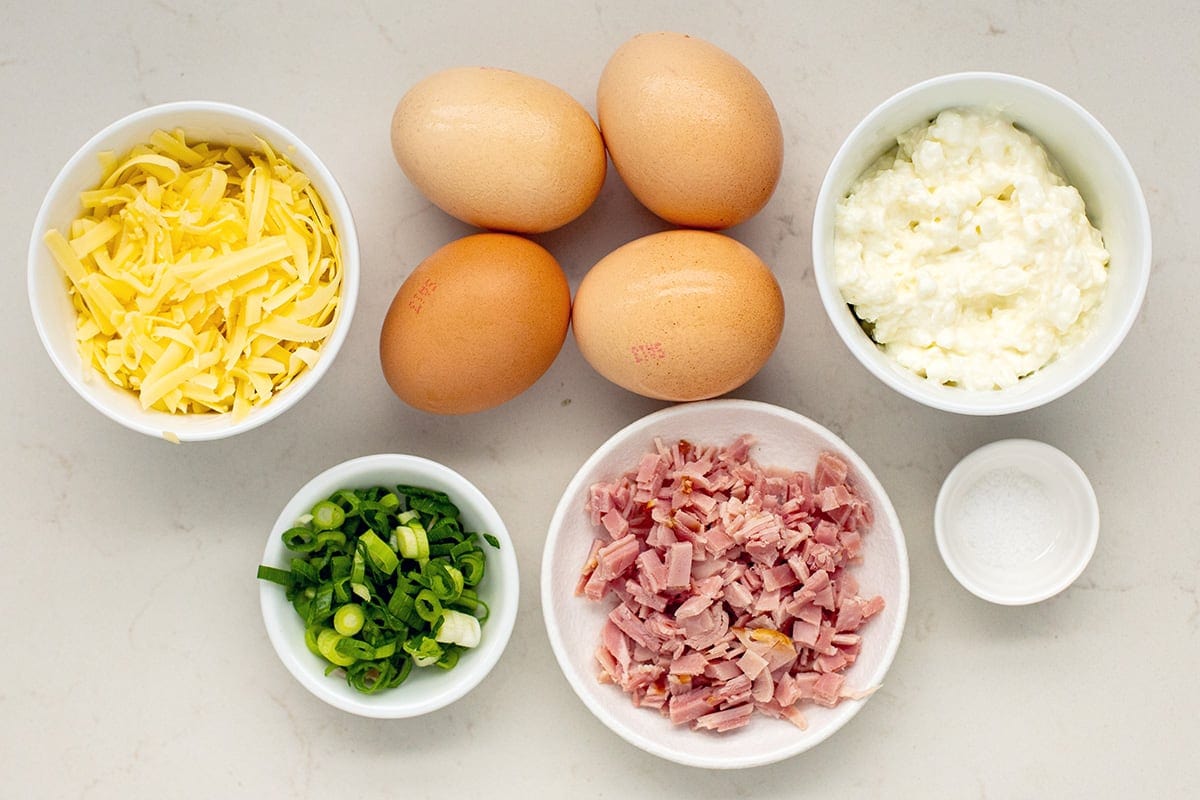Ingredients for the recipe including eggs, salt, cottage cheese, cheddar cheese, diced ham, and chopped spring onions.