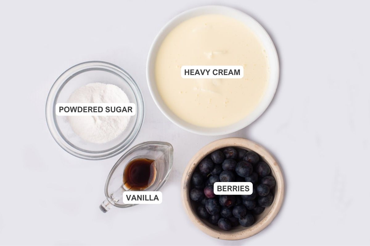 Ingredients for the whipped cream including heavy cream, berries, powdered sugar, and vanilla extract.
