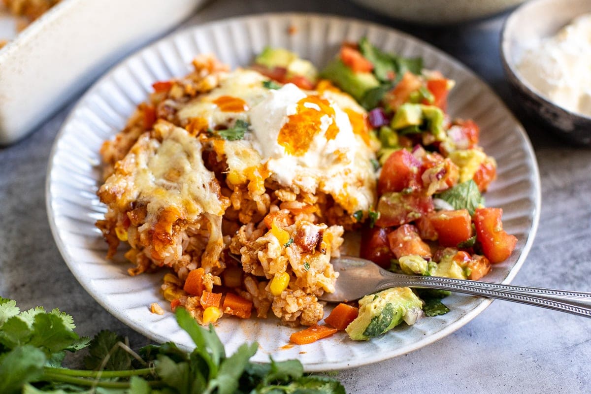 Cheesy chicken rice casserole on a plate with avocado tomato salad.