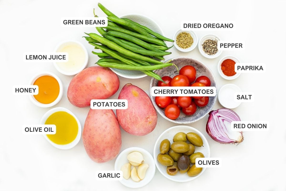 Ingredients for the recipe including potatoes, green beans, dried oregano, pepper, paprika, salt, red onion, olives, cherry tomatoes, garlic, lemon juice, honey, and olive oil.
