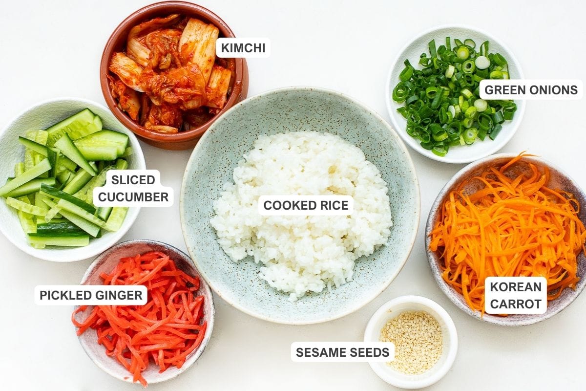 Korean beef bowl toppings: kimchi, sliced cucumber, green onions, cooked rice, korean carrot, pickled ginger, and sesame seeds.