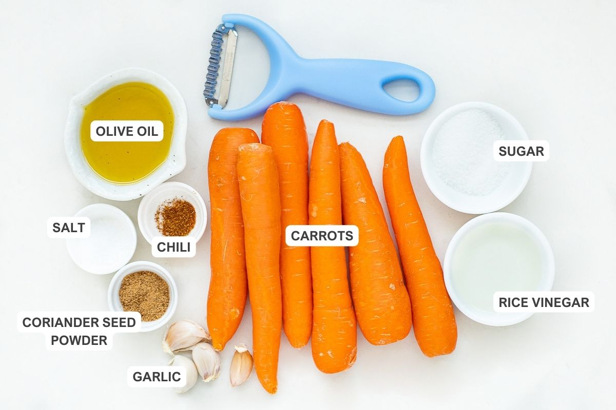 Ingredients for the recipe including carrots, olive oil, sugar, salt, chili, rice vinegar, coriander seed powder, and garlic.