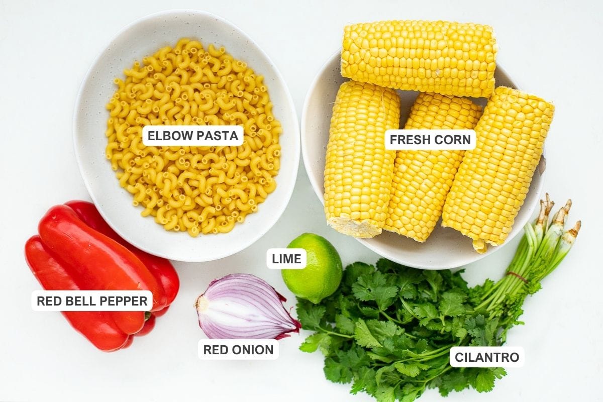 Ingredients for the recipe including fresh corn, elbow pasta, red bell pepper, lime, red onion, and cilantro.